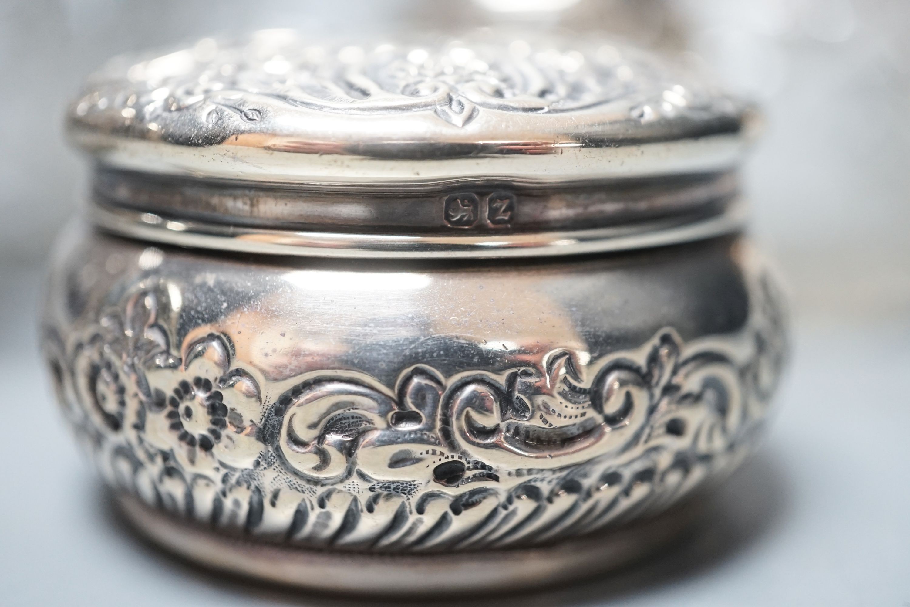 A circular embossed silver box and six silver mounted glass toilet bottles.